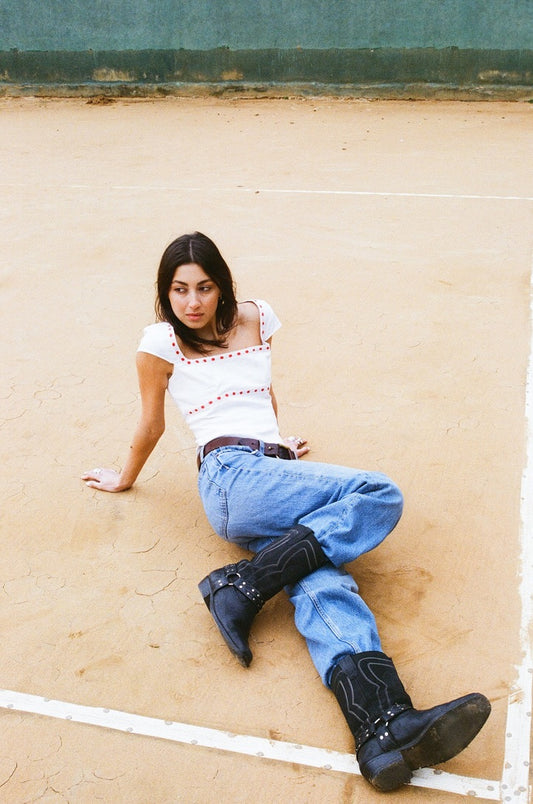 Full-length view of white linen Norma Top with red ribbon broderie anglaise trim, styled with wide-leg blue jeans, model on a street setting.