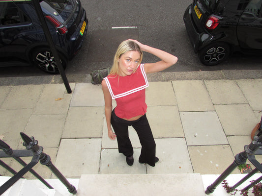Full-length view of red linen Biba Top with sailor collar and white trim, styled with wide-leg black trousers, shot outdoors against a dark background.