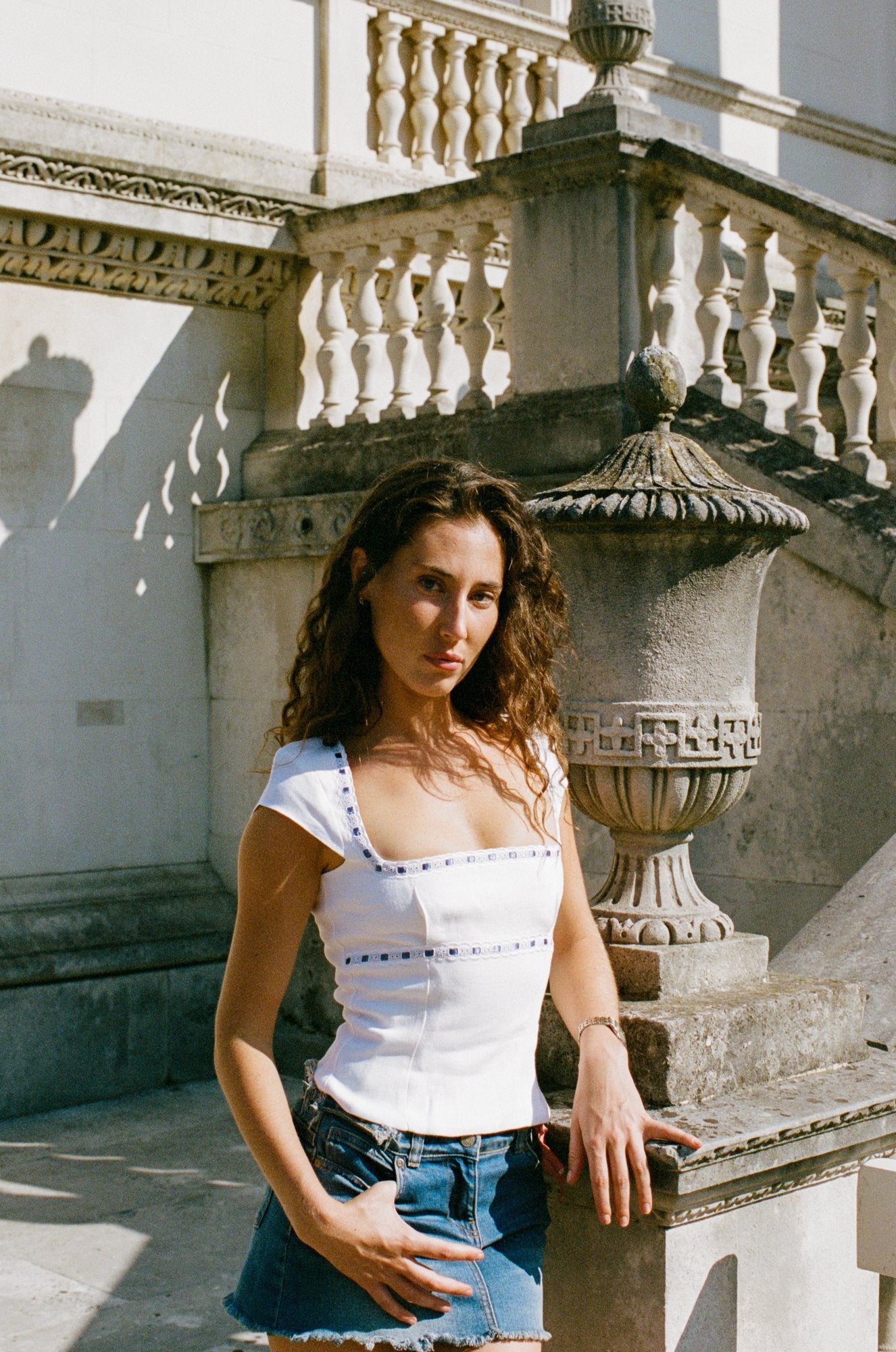 Woman wearing a white linen top with blue-ribbon broderie anglaise trim beside a stone balustrade.